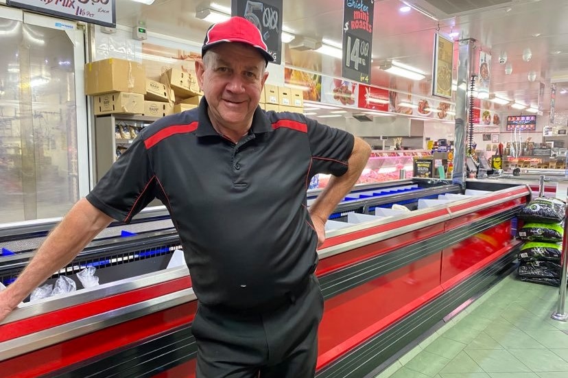 A man stands in a butcher deli and looks at the camera.