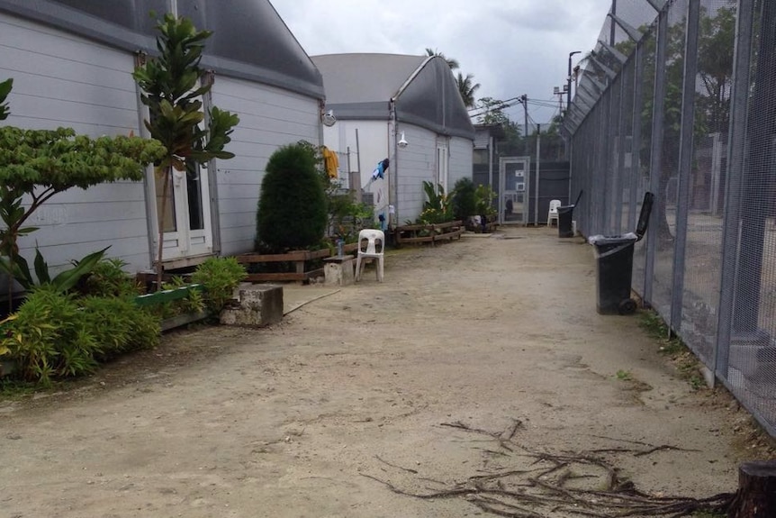 Manus Island detention centre Oscar compound buildings, inside a tall steel fence with debris on the ground.