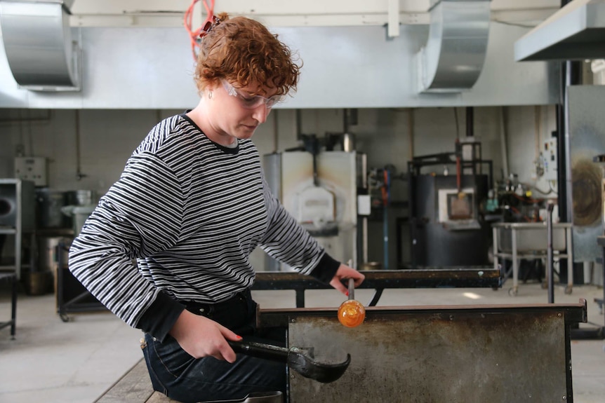 Broni holds a piece of glass at the end of a pole, it glows bright orange.