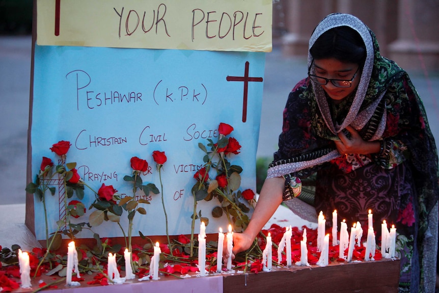 A woman drapes a shawl around her head an kneels to place a candle among red roses.