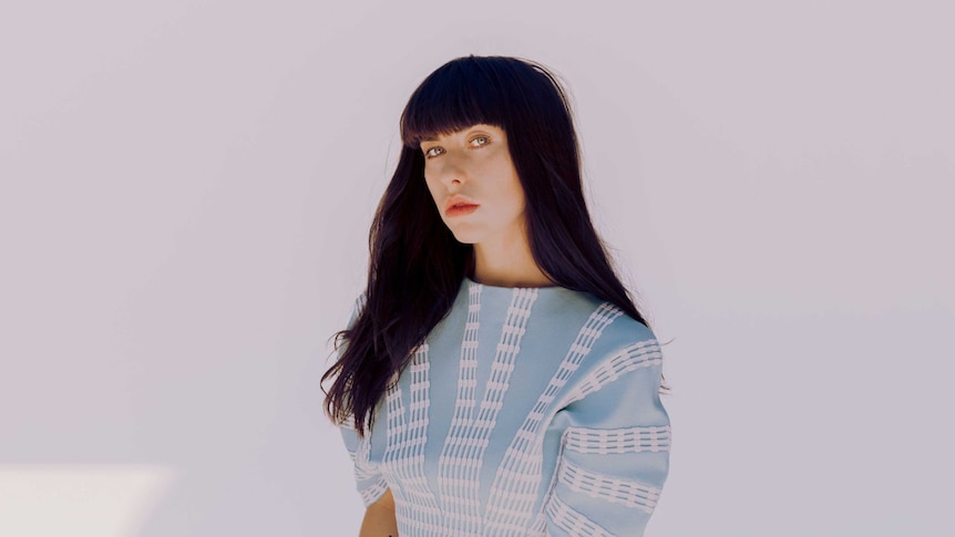 Kimbra stares down the camera in front of a soft pink background