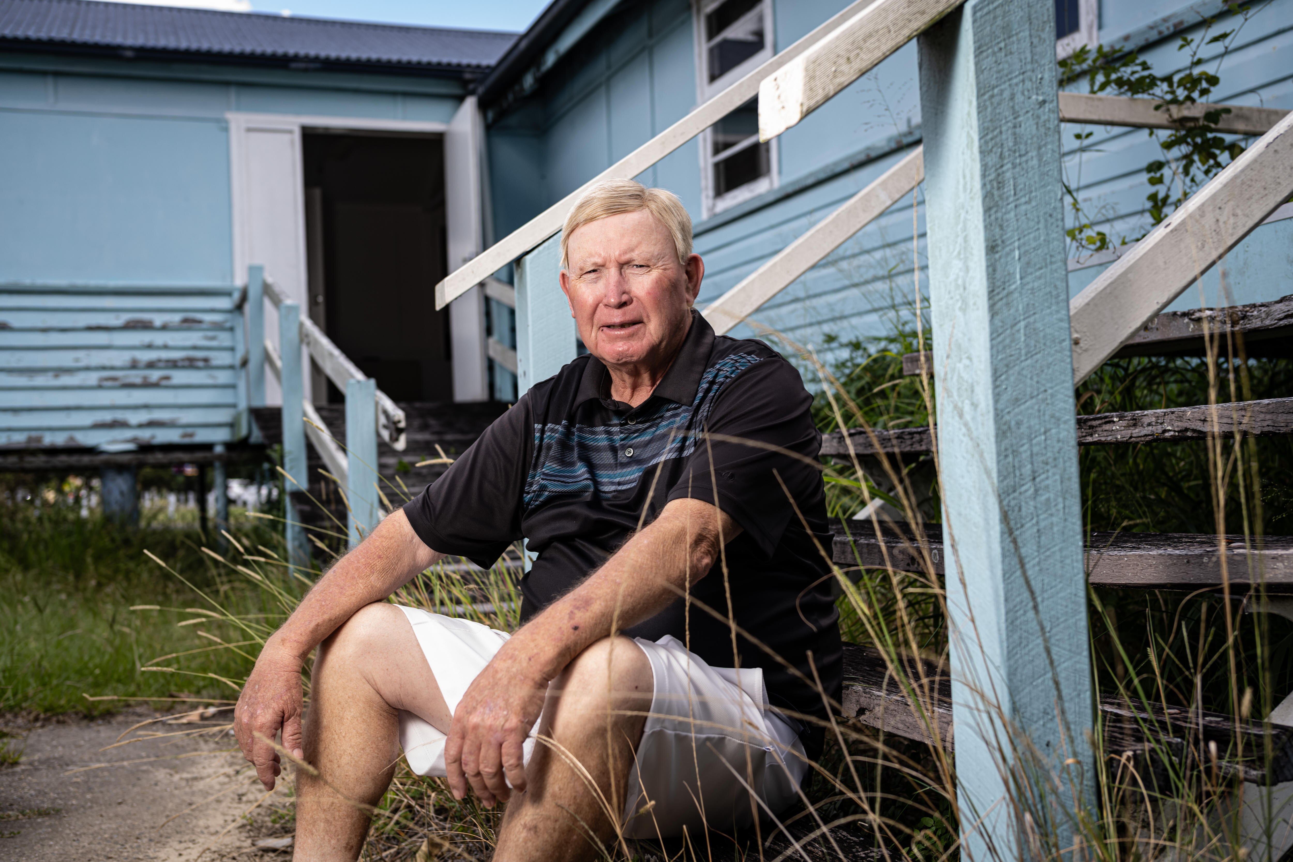 A sad man sits next to a blue building