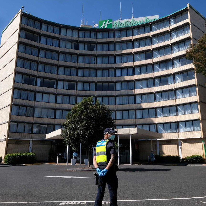 A police officer in mask and gloves sounds outside the Holiday Inn.