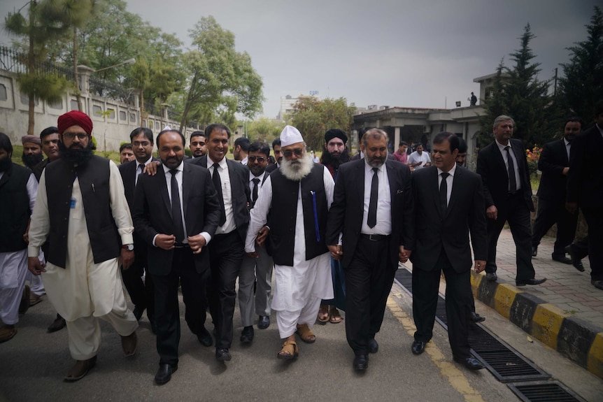 A group of Pakistani men walking down a street looking happy