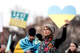 Woman holds cardboard heart at rally for victims of Ukraine crisis.