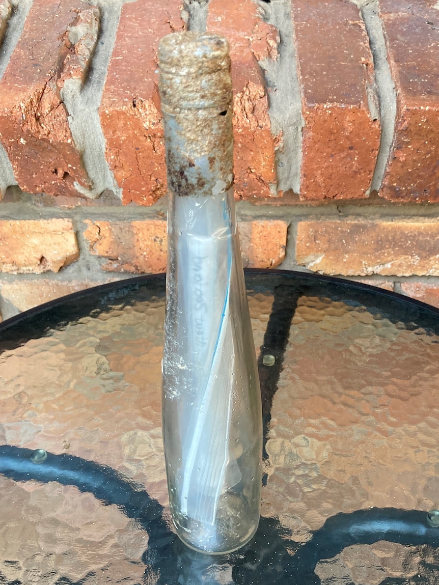 Message in a glass bottle tapped shut sitting on a table besides a brick wall