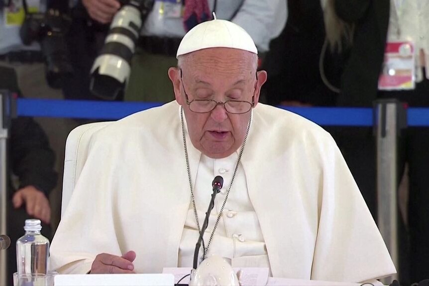 The pope speaking into a microphone at a meeting.