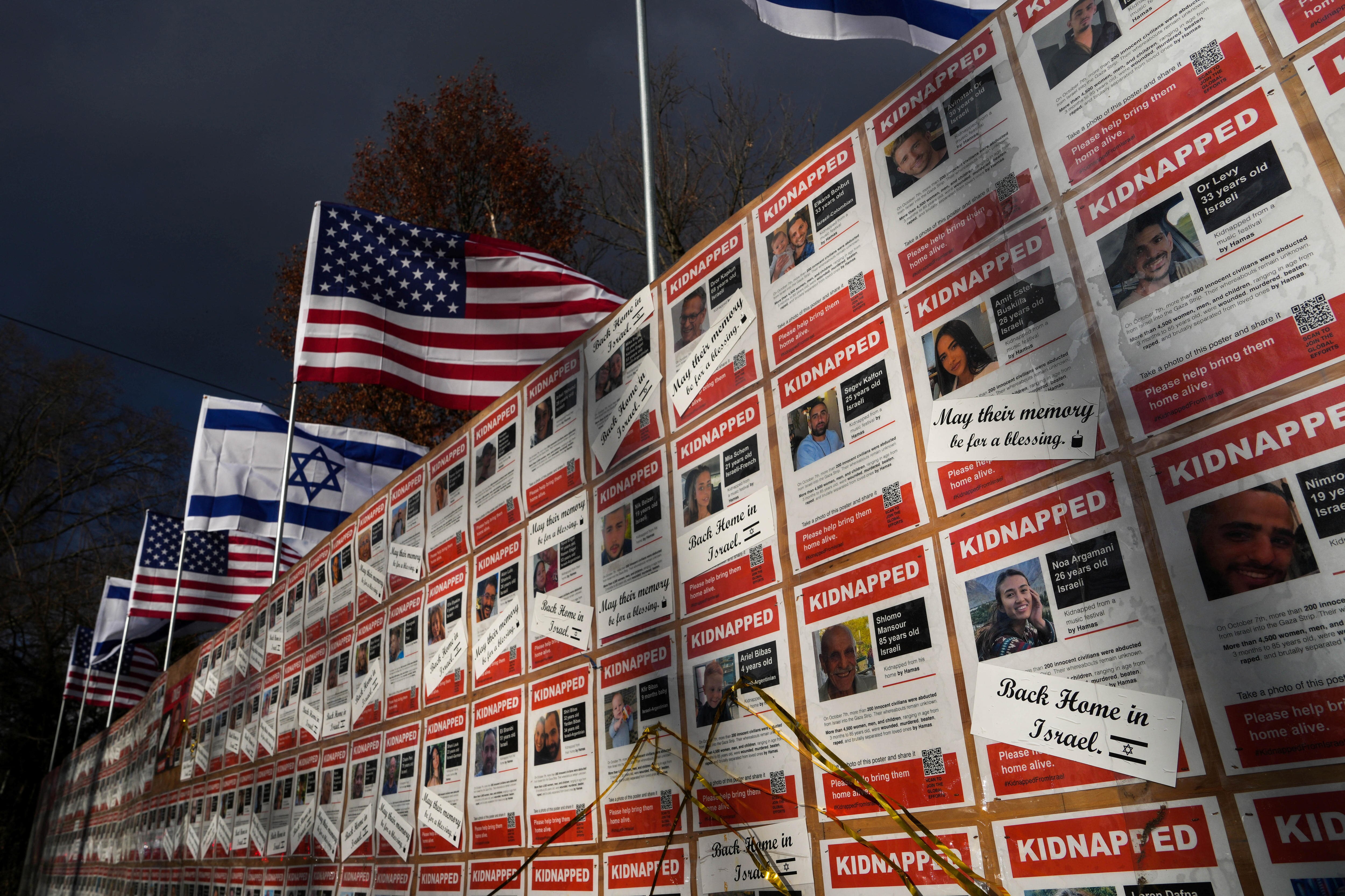 A wall of red and white posters with images of hostages' faces topped with Israeli and US flags
