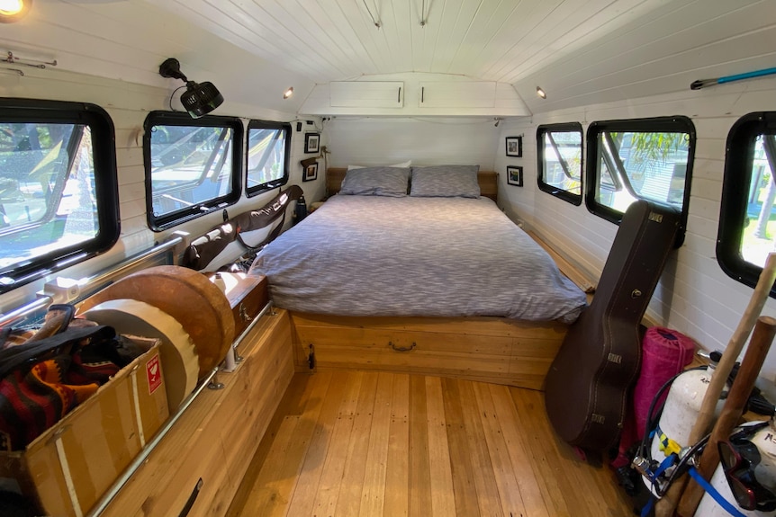 A double bed at the far end of a room built on the upper deck of a double-decker bus.