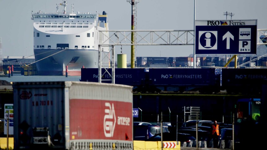A truck trailer is parked at Zeebrugge port with a large ferry in the background.
