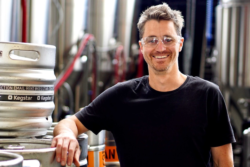 A man wearing safety glasses leans on a keg of beer.