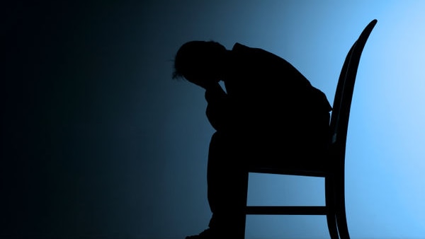 A man sitting down in a chair, with his head in his hair  silhouetted against a blue background