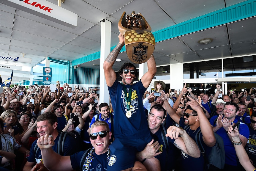 A man lifts a trophy in front of fans 