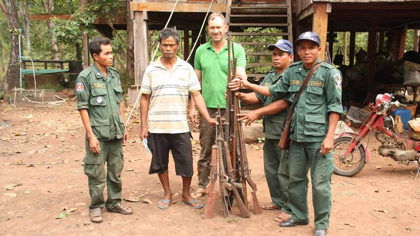 Members of Ta Bos village's Community Forest Committee and Ben Davis stand in front of a pile of confiscated guns.