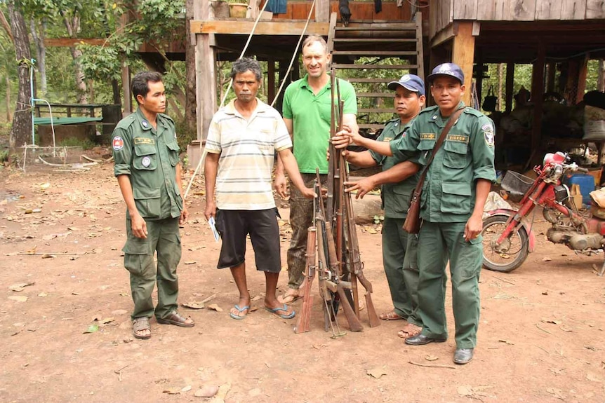 Members of Ta Bos village's Community Forest Committee and Ben Davis stand in front of a pile of confiscated guns.