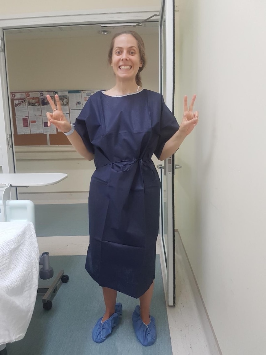 A woman wearing a navy hospital gown holding up both hands in 'peace' signs. Ausnew Home Care, NDIS registered provider, My Aged Care