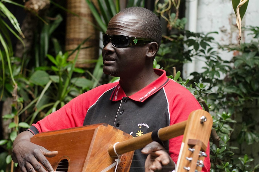 Gordon Koang holds his thom in a red and black shirt, with sunglasses on