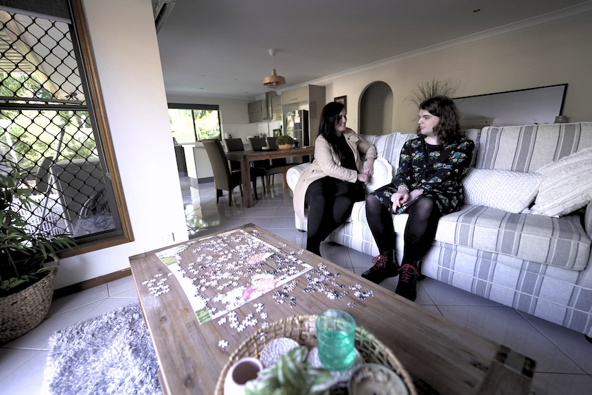 A young woman and her mother sit on a couch talking.