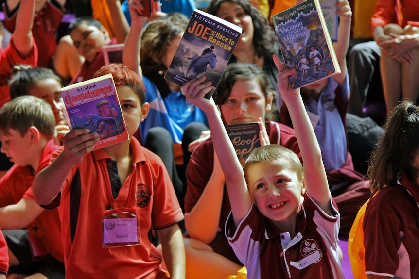 A boy holds books high in the air.