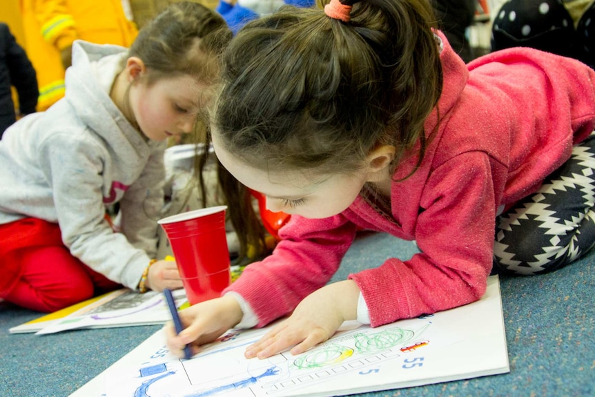 Two young girls colour in with crayons.