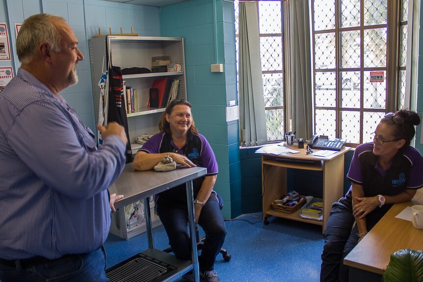 A man and two women speak with smiles on their faces in an office setting.