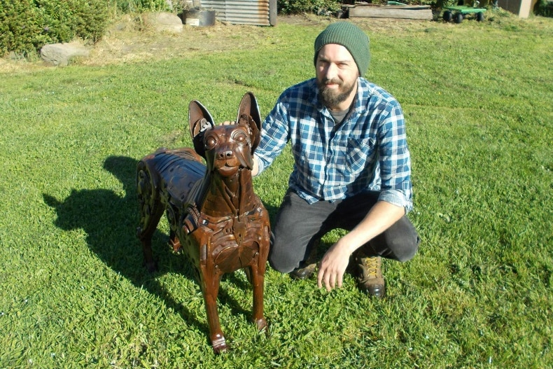 Scrap metal sculptor Matt Sloane patting the full size kelpie dog he constructed from old metal parts