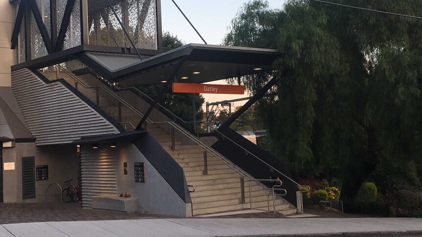 Front entrance of train station at Oatley in Sydney's south. Bunch of orange lillies on concrete seat in foreground.