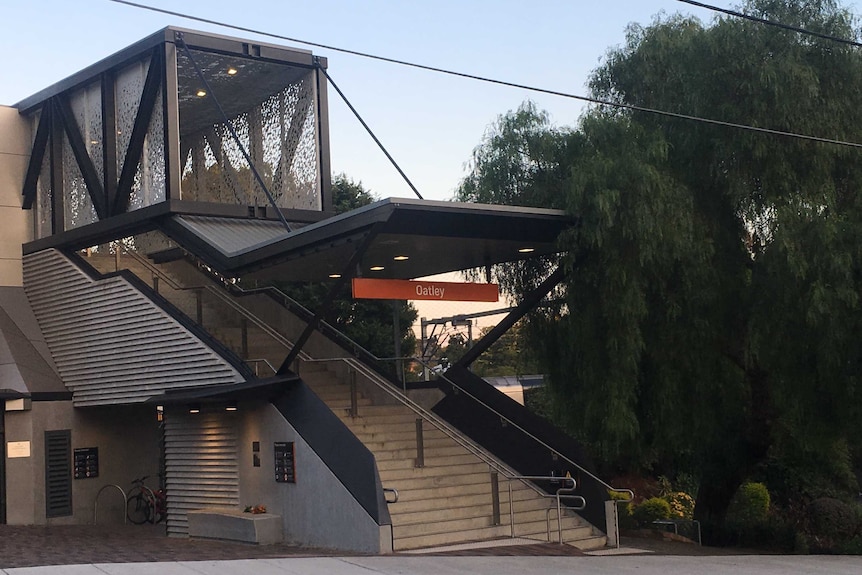 Front entrance of train station at Oatley in Sydney's south. Bunch of orange lillies on concrete seat in foreground.