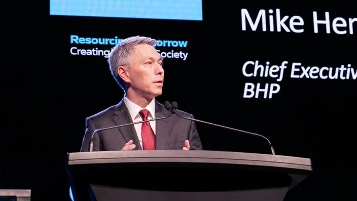 BHP chief executive Mike Henry speaks into microphones on stage at the World Mining Congress