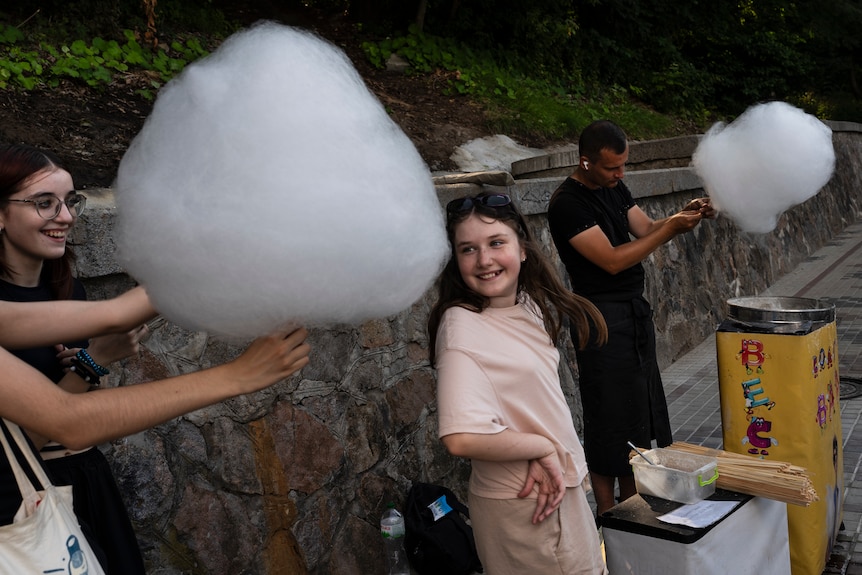 Two girls smile as one of them is handed a large portion of cotton candy