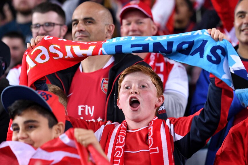 A spectator holds above his head a combined Arsenal and Sydney FC scarf prior to the start of the friendly match.