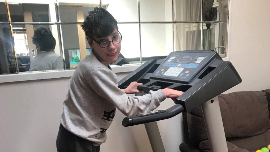 Joe Lockwood smiles while walking on a treadmill at his home where he is self-isolating with his mum.