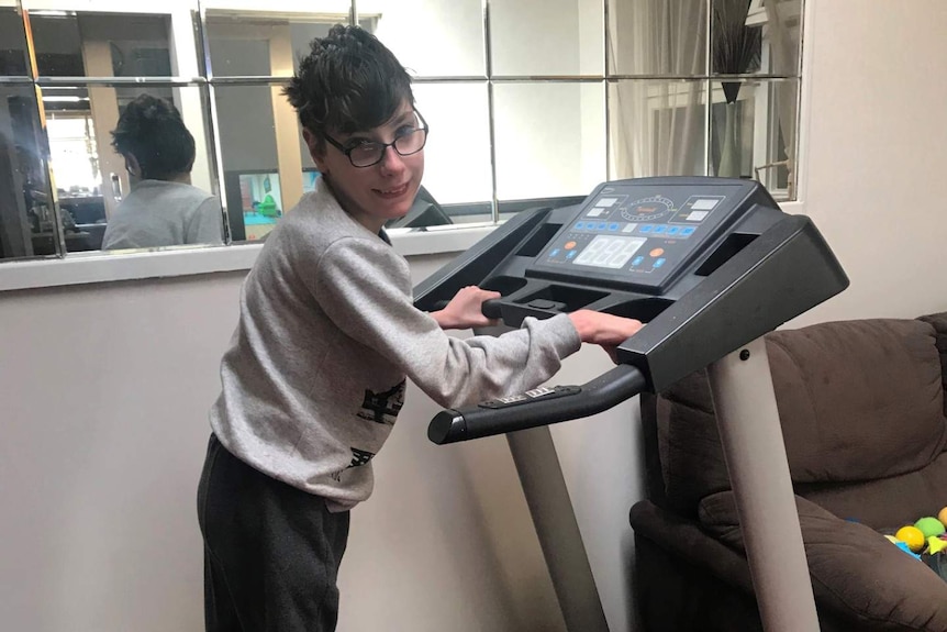 Joe Lockwood smiles while walking on a treadmill at his home where he is self-isolating with his mum.