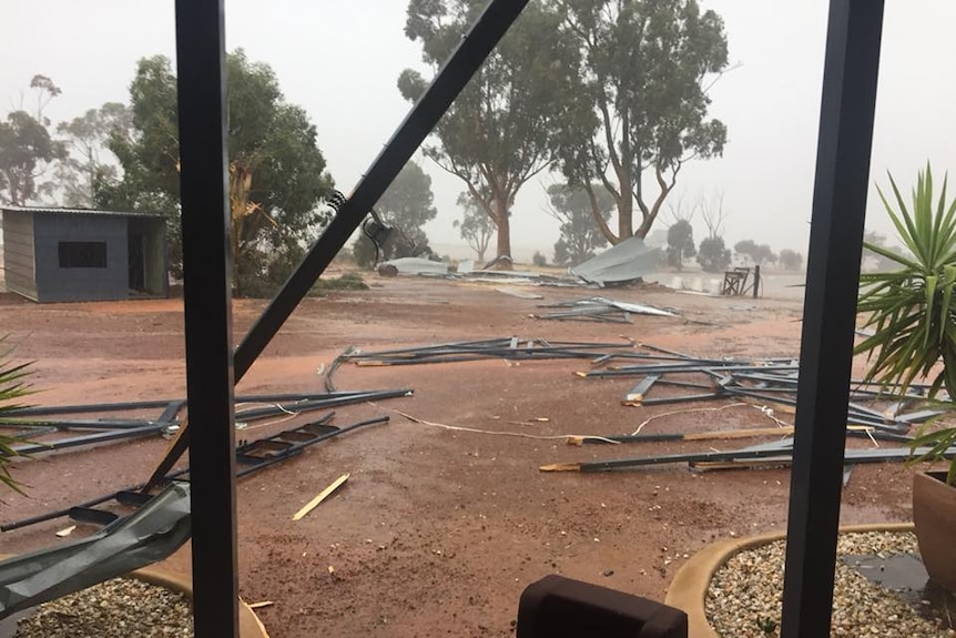 Pieces of timber and corrugated iron lie on the ground, as rain clouds hover low on the horizon.