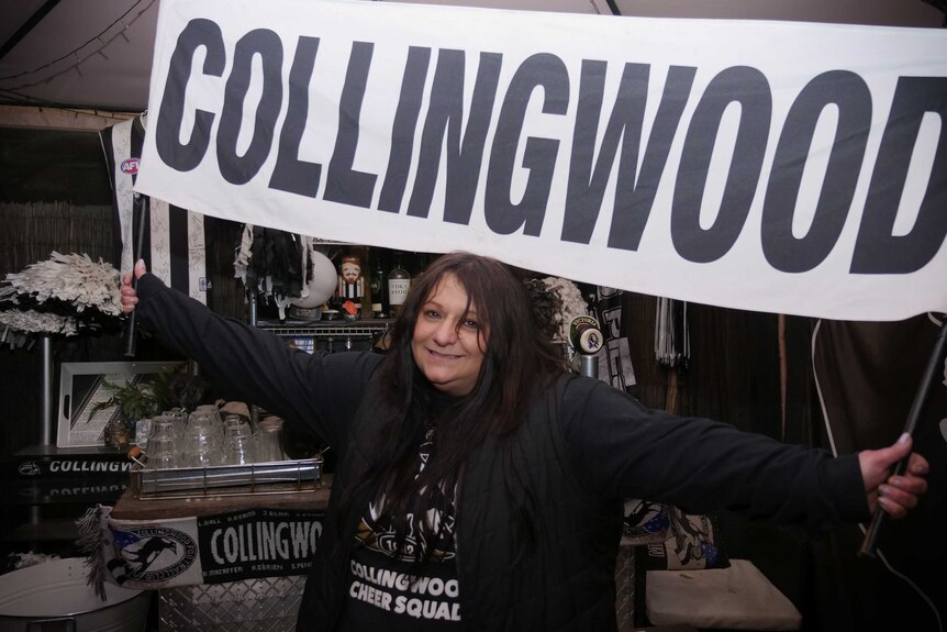 Voula Bitsikas smiles while holding up a Collingwood banner
