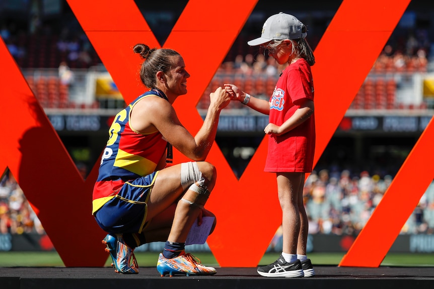 Adelaide Crows AFLW captain bends down while a child puts a medal around her neck