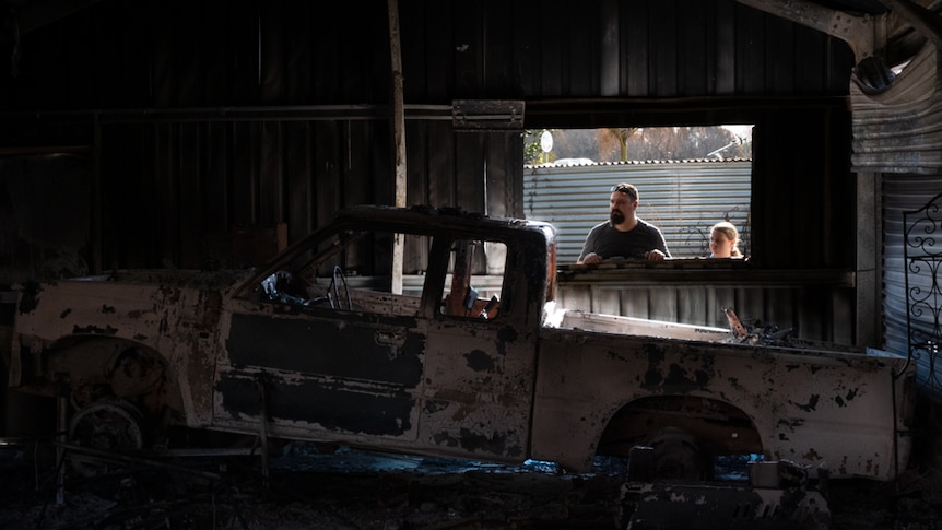 A man looks inside his burnt-out shed with his daughter standing beside him