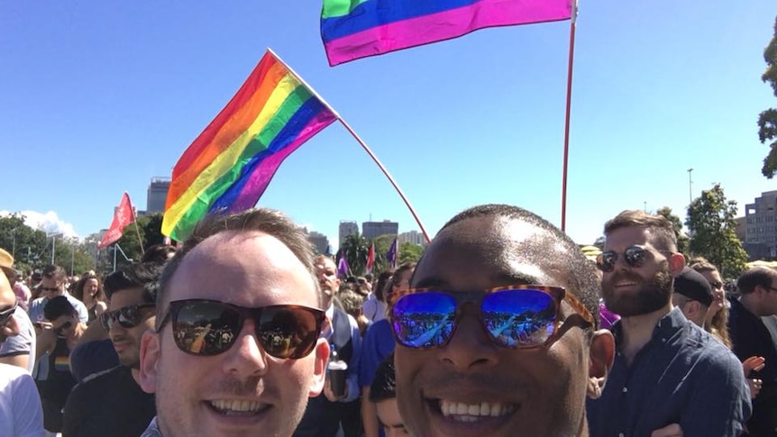 Marriage equality party Yes vote. Two men smiling in front of rainbow flags and a blue sky