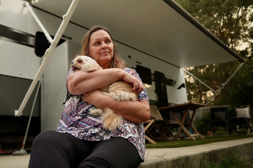 Kim Ellison hugs her dog, while sitting in front of a caravan.