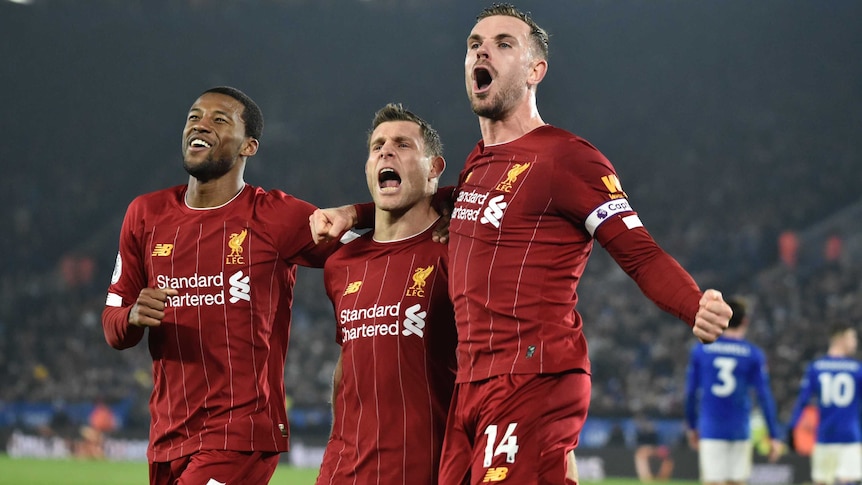 Three teammates stand calling out to fans in celebration of their team's goal in the Premier League.