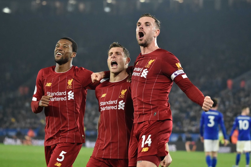 Three teammates stand calling out to fans in celebration of their team's goal in the Premier League.