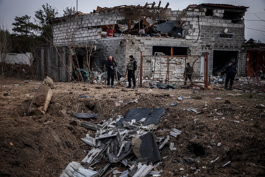 Police and residents stand next to a burnt out residential structure and nearby crater on Kyiv's outskirts, March 12, 2022.