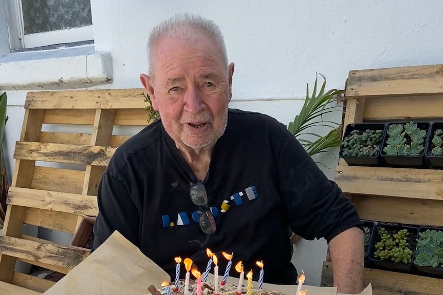 Les Twentyman sitting at a table with a birthday cake and candles. 