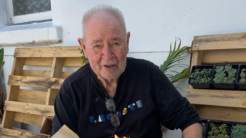 Les Twentyman sitting at a table with a birthday cake and candles. 