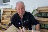 Les Twentyman sitting at a table with a birthday cake and candles. 