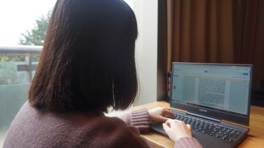 A woman with her back towards the camera is seen typing on a laptop.
