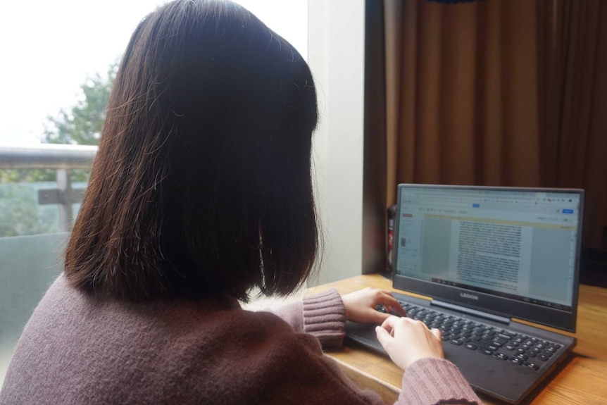 A woman with her back towards the camera is seen typing on a laptop.