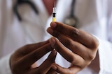 Hands holding a vaccine with a blurred figure of a person in a white coat in the background
