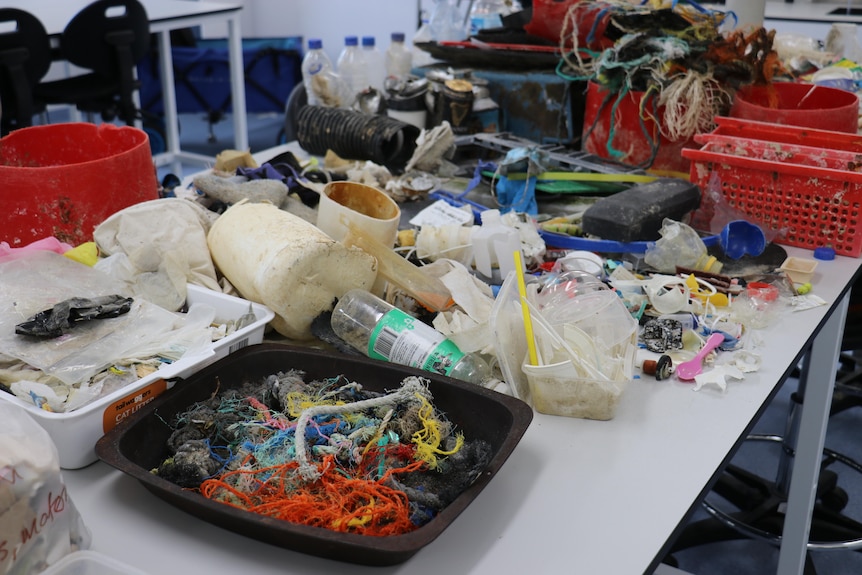 Piles of rubbish including ropes, plastic bottles and PVC pipes are sprawled out on a table.