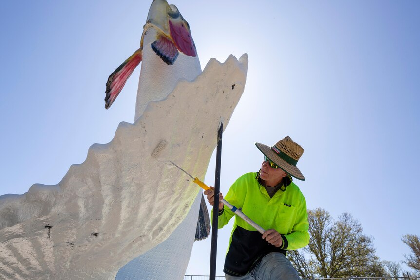 A man painting white on a big trout statue